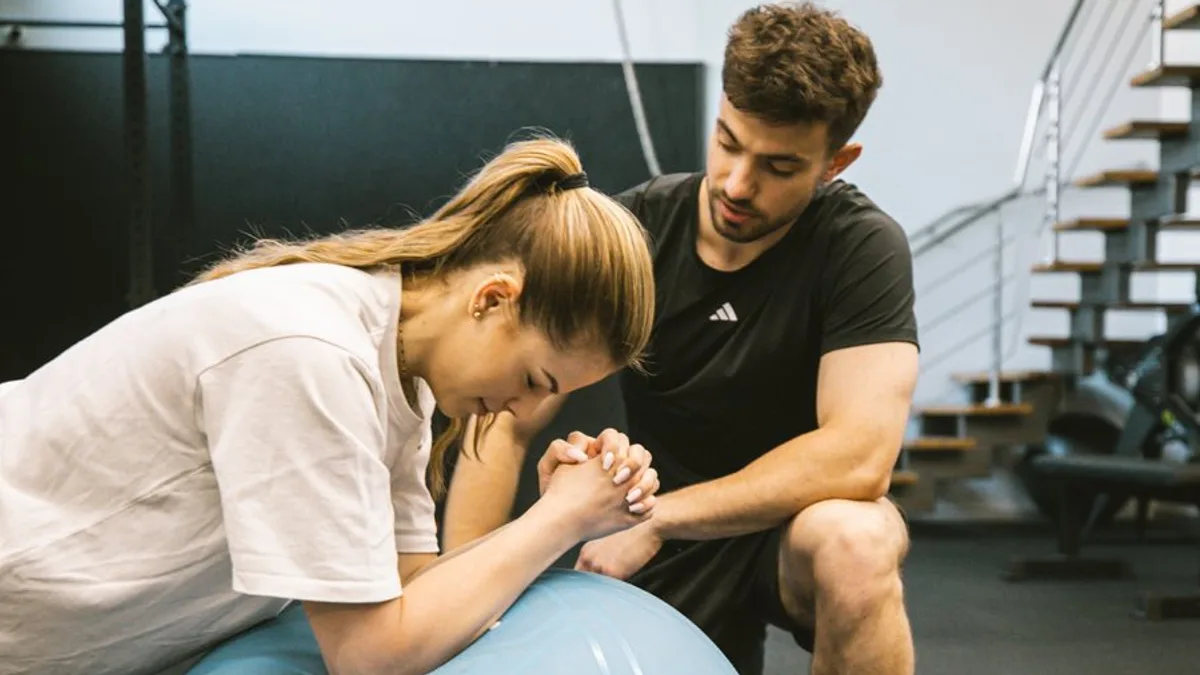 Trener personalny Jan Tekieli asekuruje klientkę podczas ćwiczenia na piłce w studiu treningowym w Krakowie